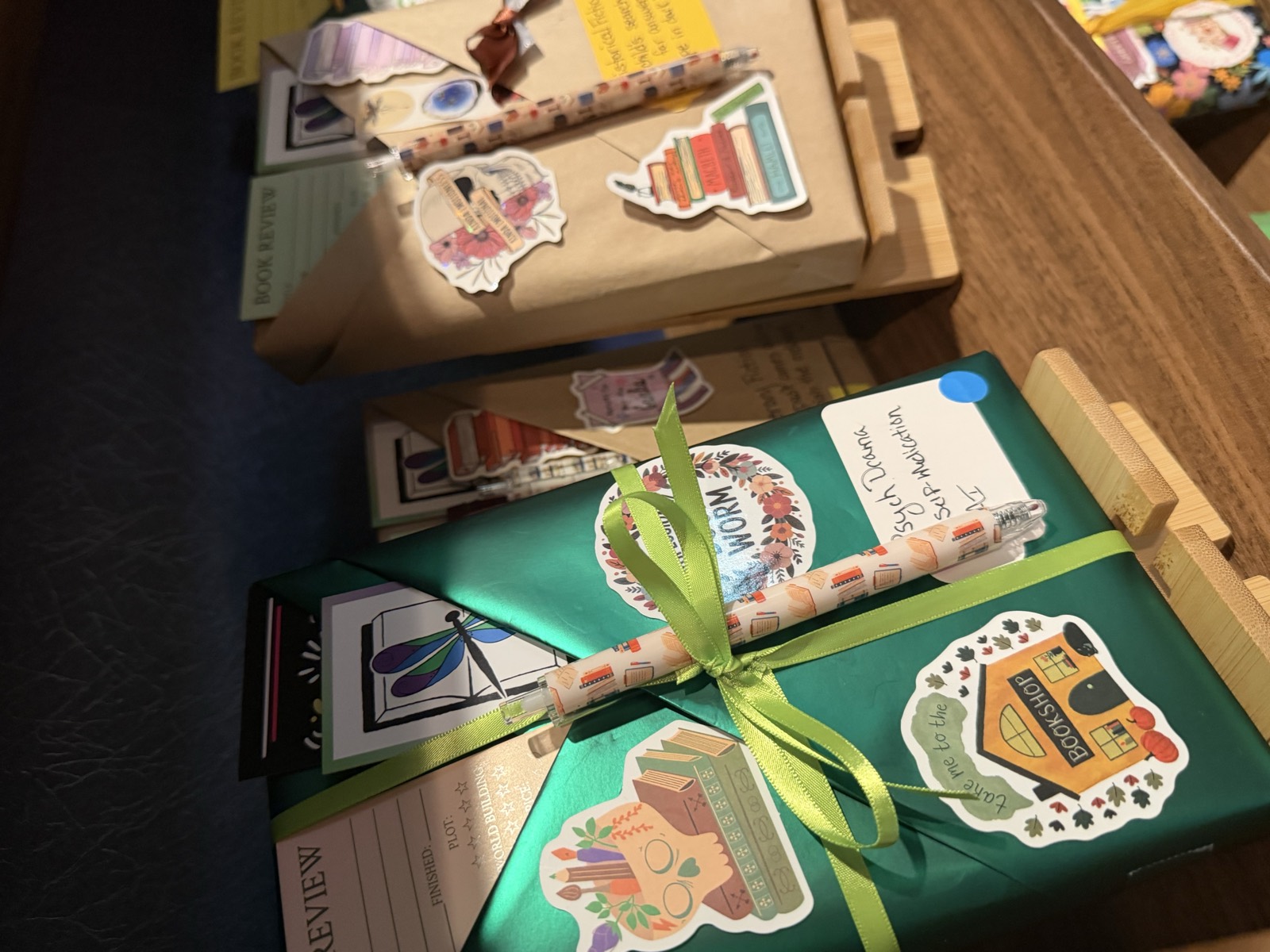 A Blind Date with a Book wrapped in metallic green paper, with handwritten clues, stickers, a patterned pen, and a dragonfly bookmark tucked in the fold.