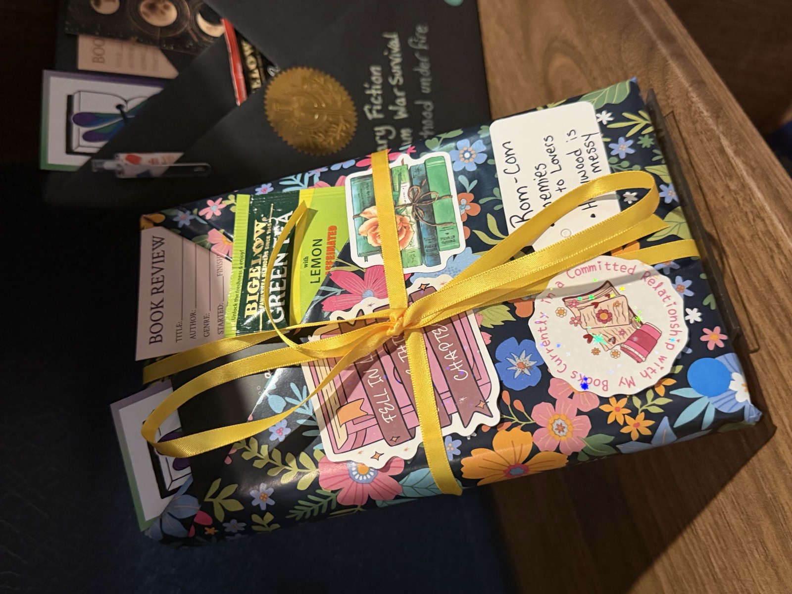 A Blind Date with a Book wrapped in navy floral paper and a yellow ribbon, with rom-com clues and a packet of tea tucked in the top.