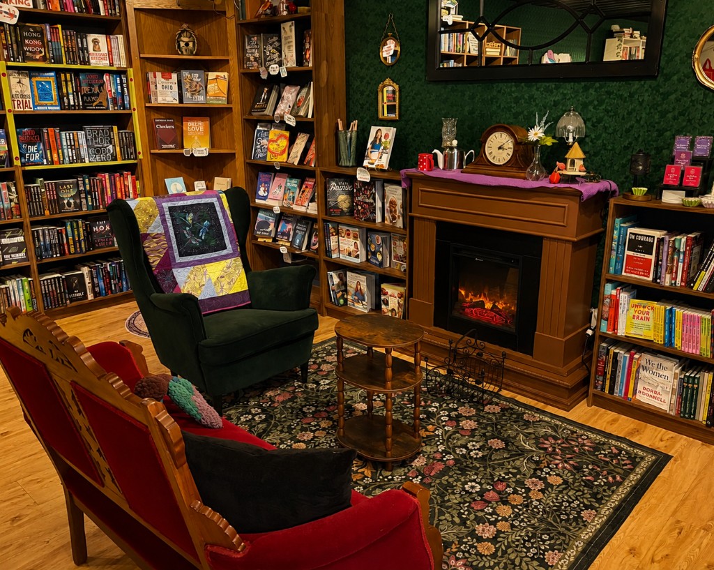 The reading nook at Dragonfly Bookshop — green wingback chair, red settee, and fireplace surrounded by bookshelves.